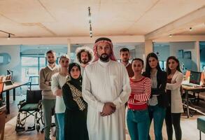 un diverso grupo de exitoso negocio personas en un moderno vaso oficina estar juntos a el parte superior con su árabe líder director foto