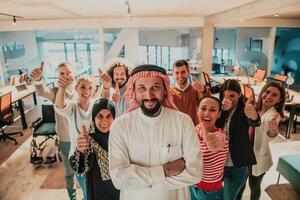 un diverso grupo de exitoso negocio personas en un moderno vaso oficina estar juntos a el parte superior con su árabe líder director foto