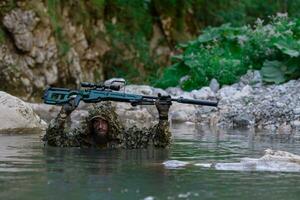 un militar hombre o airsoft jugador en un camuflaje traje furtivo el río y objetivos desde un francotirador rifle a el lado o a objetivo. foto