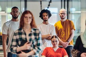 A diverse group of business people walking a corridor in the glass-enclosed office of a modern startup, including a person in a wheelchair and a woman wearing a hijab, showing a dynamic mix of innovation and unity. photo