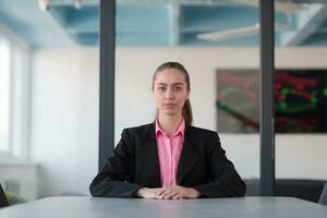 Successful young female leader in a suit with a pink shirt sitting in a modern glass office with a determined smile. photo