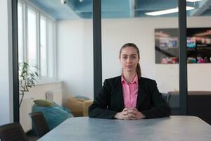 Successful young female leader in a suit with a pink shirt sitting in a modern glass office with a determined smile. photo