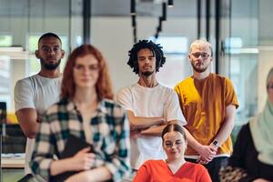 A diverse group of business people walking a corridor in the glass-enclosed office of a modern startup, including a person in a wheelchair and a woman wearing a hijab, showing a dynamic mix of innovation and unity. photo