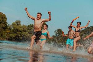 A group of diverse young people having fun together as they run along the river and play water games photo