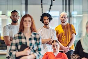 A diverse group of business people walking a corridor in the glass-enclosed office of a modern startup, including a person in a wheelchair and a woman wearing a hijab, showing a dynamic mix of innovation and unity. photo