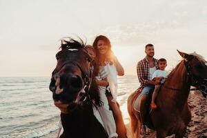 The family spends time with their children while riding horses together on a sandy beach. Selective focus photo