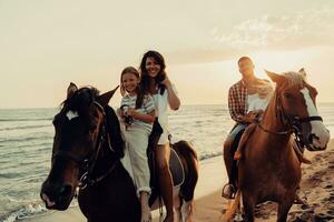 The family spends time with their children while riding horses together on a sandy beach. Selective focus photo