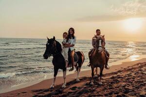 The family spends time with their children while riding horses together on a sandy beach. Selective focus photo