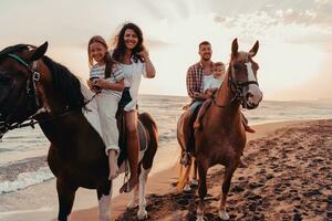 The family spends time with their children while riding horses together on a sandy beach. Selective focus photo