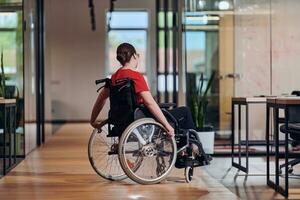 A modern young businesswoman in a wheelchair is surrounded by an inclusive workspace with glass-walled offices, embodying determination and innovation in the business world photo