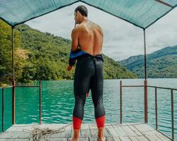 Athlete putting on a swimming suit and preparing for triathlon swimming and training in the river surrounded by natural greenery photo