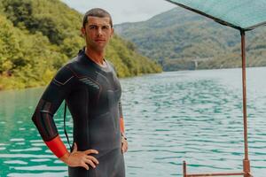 Athlete putting on a swimming suit and preparing for triathlon swimming and training in the river surrounded by natural greenery photo