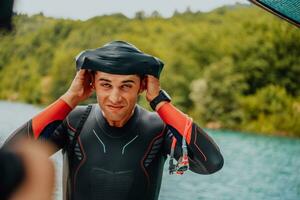 Athlete putting on a swimming suit and preparing for triathlon swimming and training in the river surrounded by natural greenery photo