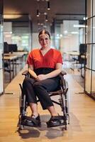 A modern young businesswoman in a wheelchair is surrounded by an inclusive workspace with glass-walled offices, embodying determination and innovation in the business world photo