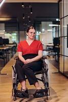 un moderno joven mujer de negocios en un silla de ruedas es rodeado por un inclusivo espacio de trabajo con con paredes de vidrio oficinas, encarnando determinación y innovación en el negocio mundo foto