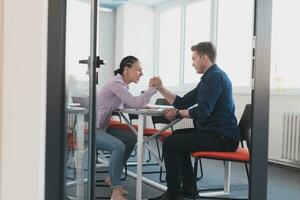 Businesspeople, rivalry and people concept - businesswoman and businessman arm wrestling during corporate meeting in modern bright open space coworking startup business office. photo