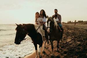 The family spends time with their children while riding horses together on a sandy beach. Selective focus photo