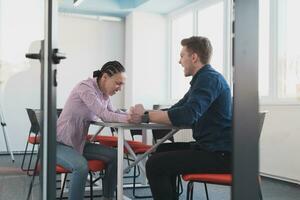 Businesspeople, rivalry and people concept - businesswoman and businessman arm wrestling during corporate meeting in modern bright open space coworking startup business office. photo