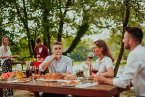 Group of happy friends having picnic french dinner party outdoor during summer holiday vacation near the river at beautiful nature photo