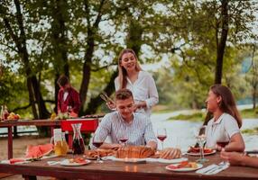 Group of happy friends having picnic french dinner party outdoor during summer holiday vacation near the river at beautiful nature photo