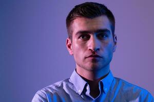 A man in a shirt poses on a dark multicolored neon background photo