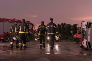 valiente bomberos equipo caminando a el cámara. en antecedentes paramédicos y bomberos rescate equipo lucha fuego en coche accidente, seguro y salvar pueblos vive concepto. foto