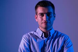 A man in a shirt poses on a dark multicolored neon background photo