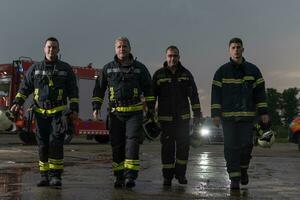 valiente bomberos equipo caminando a el cámara. en antecedentes paramédicos y bomberos rescate equipo lucha fuego en coche accidente, seguro y salvar pueblos vive concepto. foto