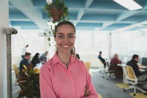 retrato de joven sonriente negocio mujer en creativo abierto espacio trabajo colaborativo puesta en marcha oficina. exitoso mujer de negocios en pie en oficina con espacio de copia. compañeros de trabajo trabajando en antecedentes. foto