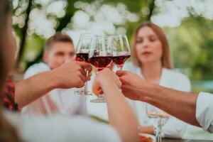 grupo de contento amigos tostado rojo vino vaso mientras teniendo picnic francés cena fiesta al aire libre durante verano fiesta vacaciones cerca el río a hermosa naturaleza foto