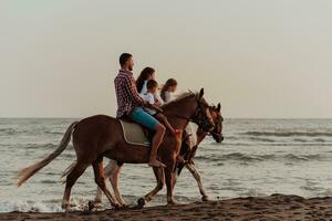 The family spends time with their children while riding horses together on a sandy beach. Selective focus photo