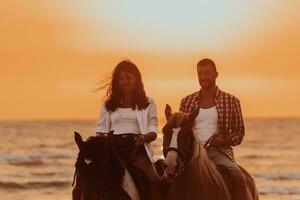 A loving couple in summer clothes riding a horse on a sandy beach at sunset. Sea and sunset in the background. Selective focus photo