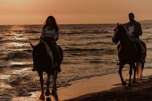 una pareja amorosa vestida de verano montando a caballo en una playa de arena al atardecer. mar y puesta de sol de fondo. enfoque selectivo foto