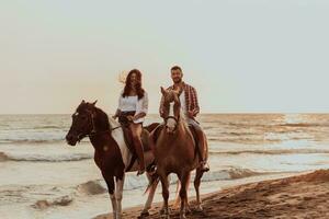 A loving couple in summer clothes riding a horse on a sandy beach at sunset. Sea and sunset in the background. Selective focus photo