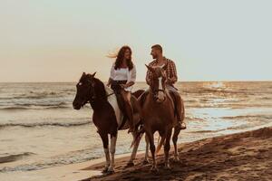 A loving couple in summer clothes riding a horse on a sandy beach at sunset. Sea and sunset in the background. Selective focus photo