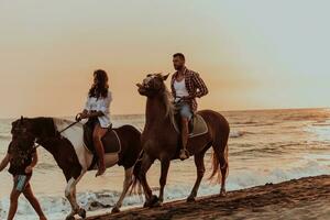 A loving couple in summer clothes riding a horse on a sandy beach at sunset. Sea and sunset in the background. Selective focus photo