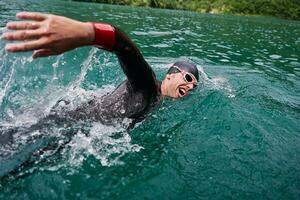 triathlon athlete swimming on lake wearing wetsuit photo