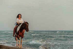 Woman in summer clothes enjoys riding a horse on a beautiful sandy beach at sunset. Selective focus photo