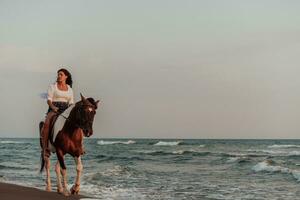 Woman in summer clothes enjoys riding a horse on a beautiful sandy beach at sunset. Selective focus photo