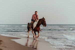 un hombre moderno con ropa de verano disfruta montando a caballo en una hermosa playa de arena al atardecer. enfoque selectivo foto