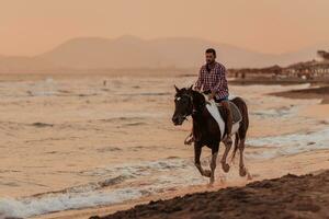 un hombre moderno con ropa de verano disfruta montando a caballo en una hermosa playa de arena al atardecer. enfoque selectivo foto