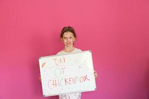 A little schoolgirl with chickenpox draws a message on the whiteboard in the kids' room, and antiseptic cream is applied to the face and body. Chalkboard background. photo