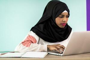 African American girl wearing a hijab is disappointed and sad sitting in her home office and using a laptop photo