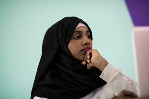 African American girl wearing a hijab is disappointed and sad sitting in her home office and using a laptop photo