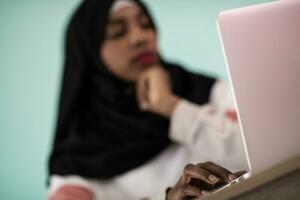 afro girl wearing a hijab is disappointed and sad sitting in her home office and using a laptop photo