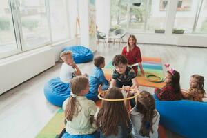 un contento hembra profesor sentado y jugando mano juegos con un grupo de pequeño Niños de escuela foto