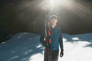 Portrait handsome male athlete with cross country skis in hands and goggles, training in snowy forest. Healthy winter lifestyle concept. photo