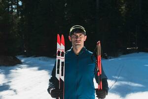 Portrait handsome male athlete with cross country skis in hands and goggles, training in snowy forest. Healthy winter lifestyle concept. photo