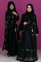 Two beautiful muslim woman in fashinable dress with hijab isolated on modern pink background representing concept of modern islam and ramadan kareem photo