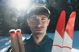 Portrait handsome male athlete with cross country skis in hands and goggles, training in snowy forest. Healthy winter lifestyle concept. photo